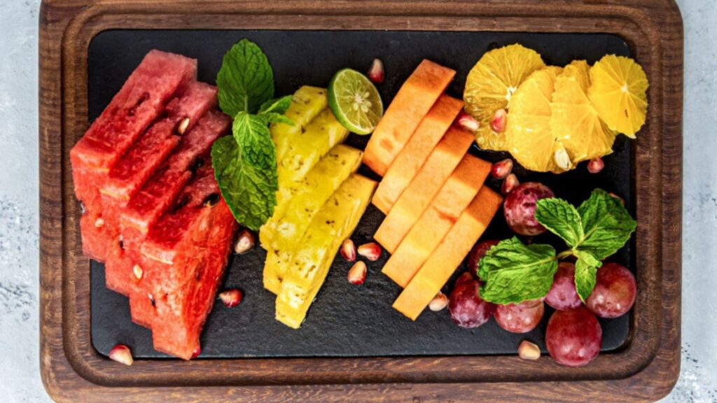 A wood plate contains watermelon carrot, and blueberry.