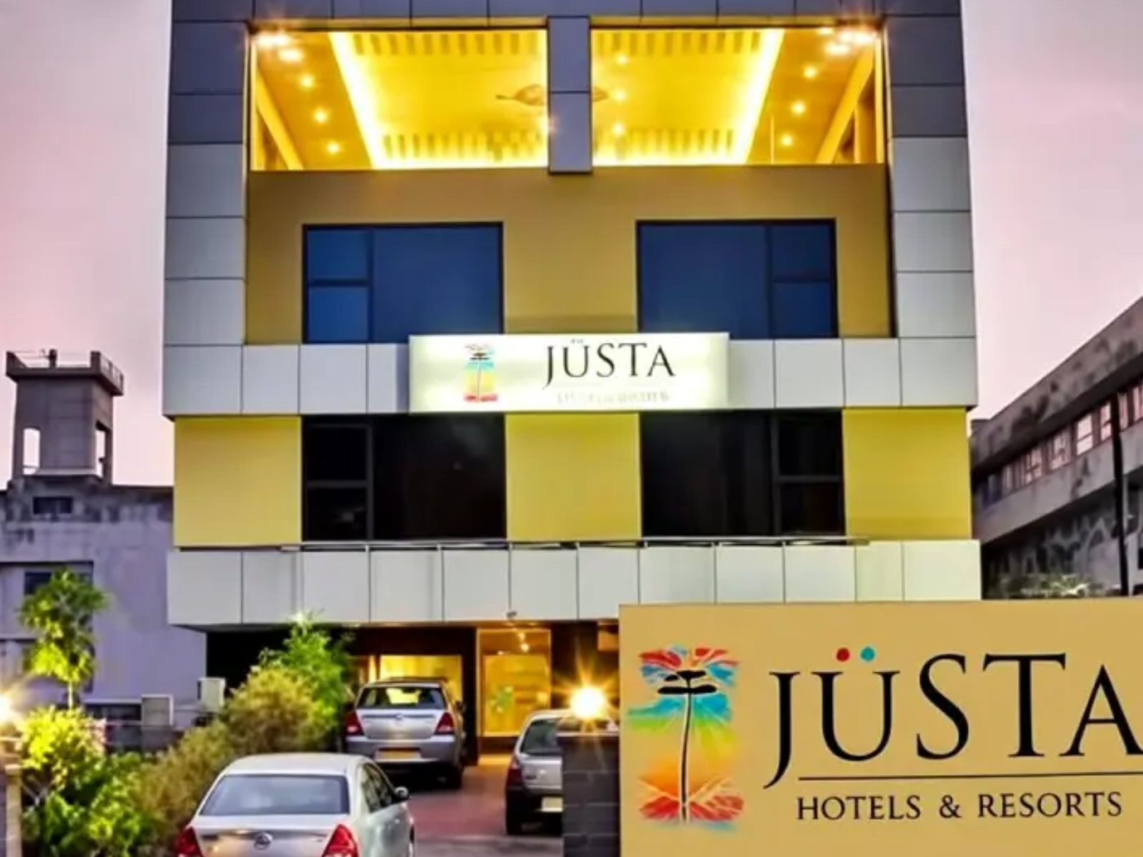 The photo highlights the exterior of the hotel with its illuminated entrance, brand signage, and parking area to attract potential guests.
